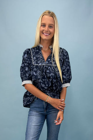 Woman wearing a navy floral blouse and jeans against a light blue background