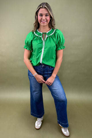 Woman wearing a green blouse with white trim and blue jeans on a beige background