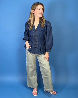 Dark wash denim peplum top featuring a notched neckline, puff sleeves, statement knotted front closures, and a flattering fitted waist.