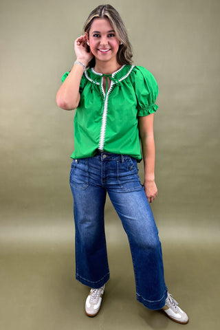 Woman wearing a green blouse with white zipper and blue jeans on a beige background