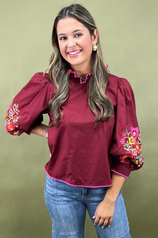 Woman wearing a burgundy blouse with colorful floral embroidery on a green background