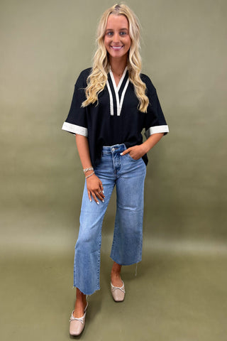 Woman wearing a black top with white trim and blue jeans on a green background