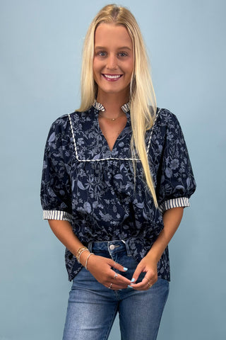 Woman wearing a dark floral blouse and jeans against a light blue background