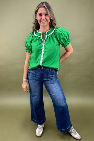 Woman wearing a green blouse with puffed sleeves and blue jeans on a beige background