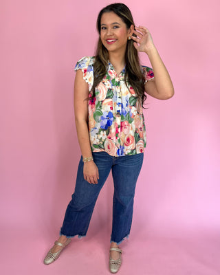 Woman wearing a floral blouse and jeans against a pink background