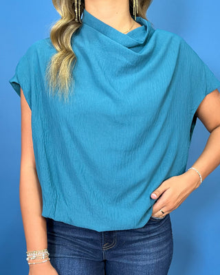 a teal short-sleeve draped top and dark blue jeans