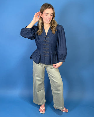 Dark wash denim peplum top featuring a notched neckline, puff sleeves, statement knotted front closures, and a flattering fitted waist.