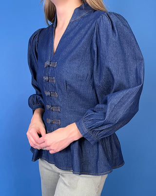 Dark wash denim peplum top featuring a notched neckline, puff sleeves, statement knotted front closures, and a flattering fitted waist.