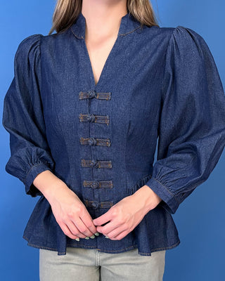 Dark wash denim peplum top featuring a notched neckline, puff sleeves, statement knotted front closures, and a flattering fitted waist.