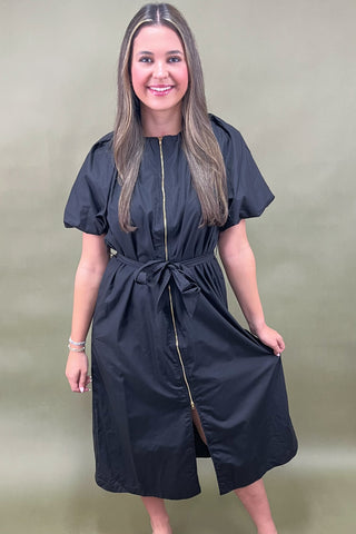 Woman wearing a black dress with a gold zipper on a beige background