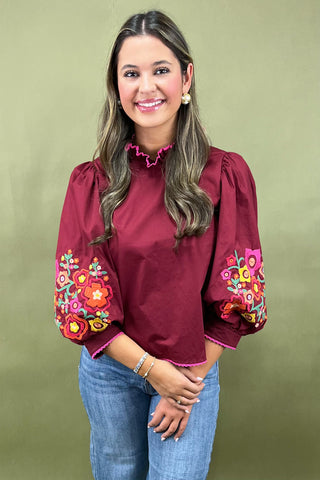 Woman wearing a burgundy blouse with colorful floral embroidery on a green background