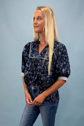 Woman wearing a navy floral blouse and jeans against a light blue background