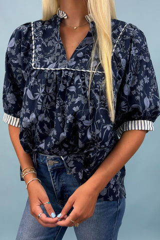 Person wearing a navy floral blouse with white trim against a light blue background