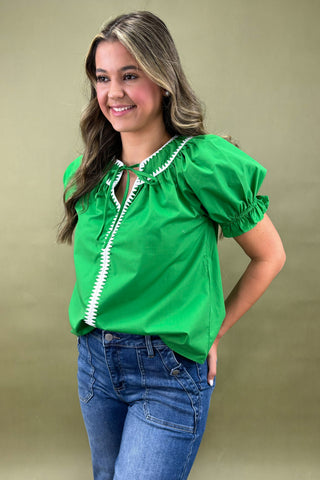 Woman wearing a green blouse with white trim against a beige background