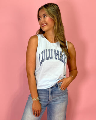 Woman wearing a white tank top with text and blue jeans against a pink background