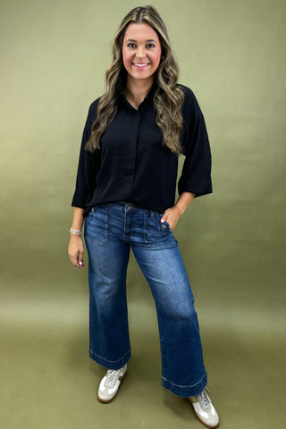 Woman wearing a black shirt and blue jeans against a green background