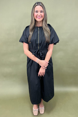 Woman wearing a black jumpsuit against a green background