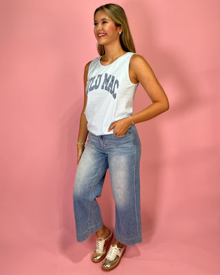 Woman wearing a white tank top with text and blue jeans against a pink background