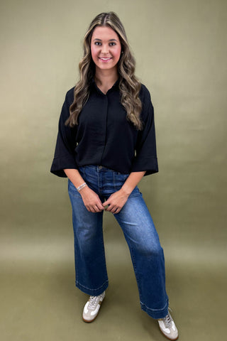 Woman wearing a black shirt and blue jeans against a green background