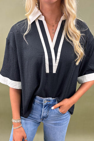 Woman wearing a navy blue top with white trim and blue jeans against a beige background