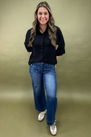 Woman wearing a black shirt and blue jeans against a green background