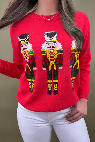 Red sweater with nutcracker design worn by a person against a brown background