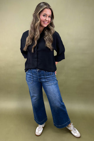 Woman wearing a black shirt and blue jeans against a green background