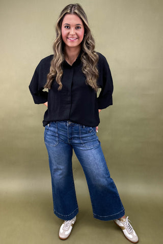 Woman wearing a black shirt and blue jeans against a green background