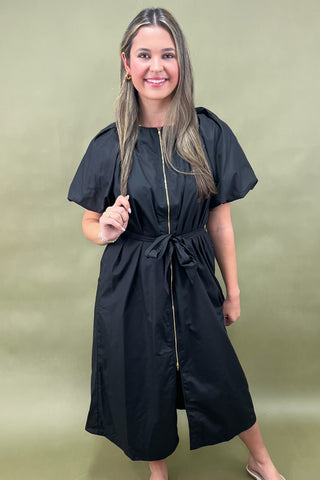 Woman wearing a black dress with a gold zipper on a green background