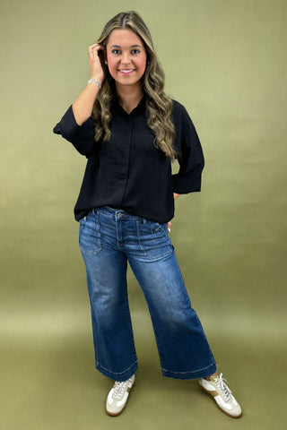 Woman wearing a black shirt and blue jeans against a green background