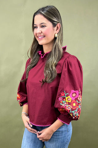 Woman wearing a burgundy blouse with floral embroidery on a beige background