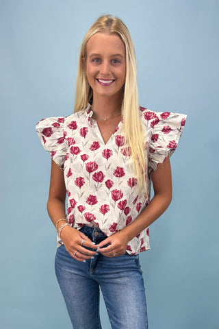 Woman wearing a floral blouse with ruffled sleeves against a light blue background