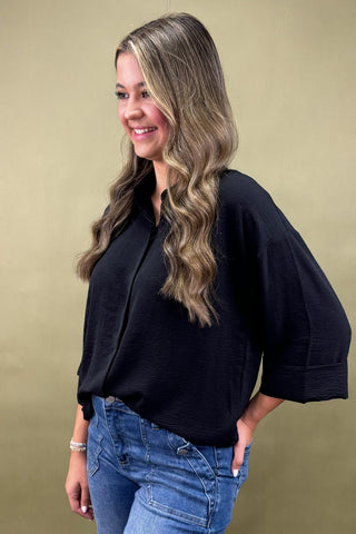 Woman wearing a black top and blue jeans against a beige background