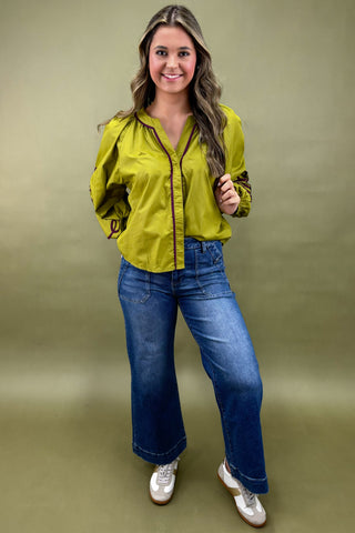Woman wearing a green blouse and blue jeans against a plain background