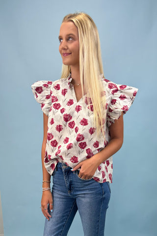 Woman wearing a floral blouse with ruffled sleeves against a blue background
