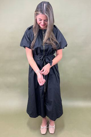 Woman wearing a black dress with a belt against a beige background