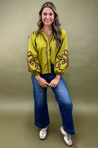 Woman wearing a bright green jacket with brown patterns and blue jeans on a beige background