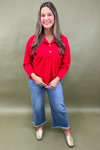 Woman wearing a red blouse and blue jeans against a plain background