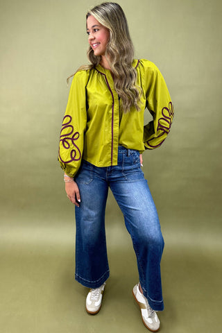 Woman wearing a bright yellow jacket with black patterns and blue jeans on a beige background