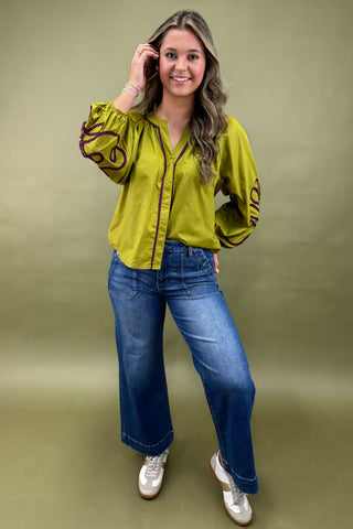 Woman wearing a green blouse with long sleeves and blue jeans on a green background