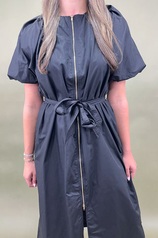 Person wearing a dark blue dress with a belt on a plain background