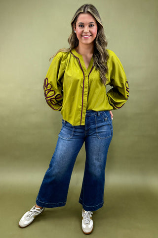 Woman wearing a bright green blouse with long sleeves and blue jeans on a green background