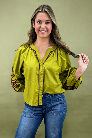 Woman wearing a green blouse with long sleeves and blue jeans against a green background