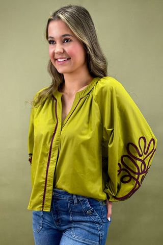 Woman wearing a green blouse with floral embroidery on a beige background