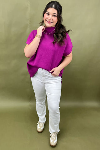 Woman wearing a purple top and white pants against a green background