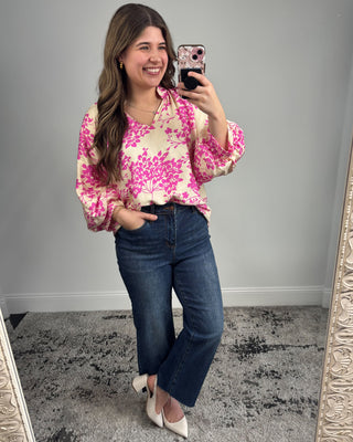 Woman taking a mirror selfie wearing a pink floral blouse and blue jeans.