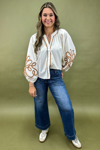 Woman wearing a white blouse with brown floral patterns and blue jeans on a green background