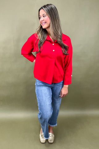 Woman wearing a red shirt and blue jeans against a beige background