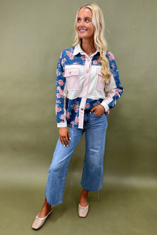 Woman wearing a floral shirt over a white blouse with blue jeans on a green background