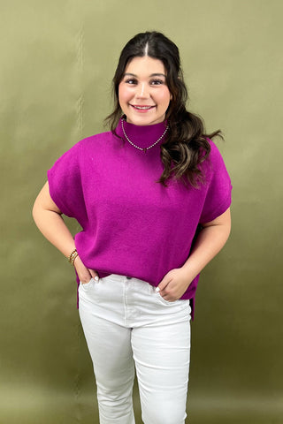 Woman wearing a bright pink sweater and white pants against a green background